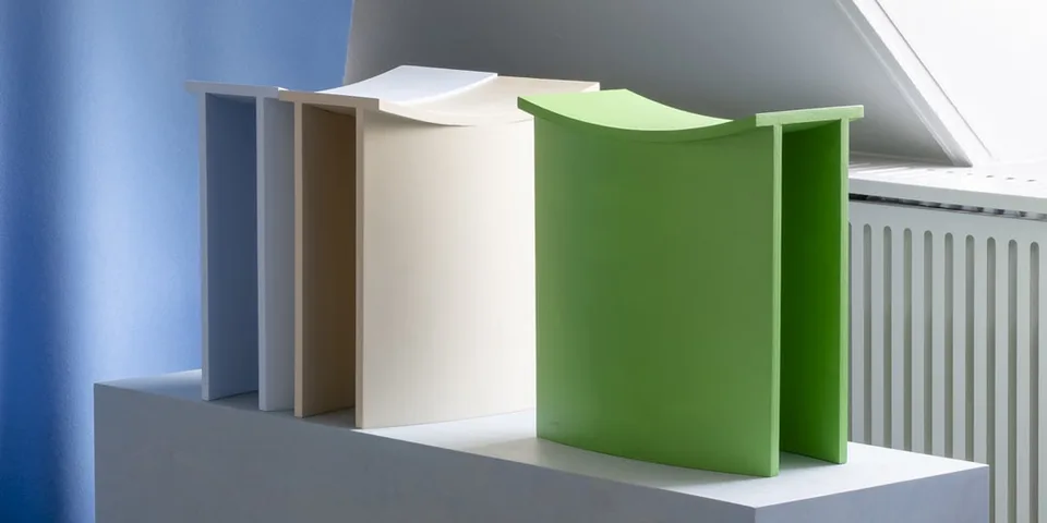 Trois sculptures modernes de couleurs pastel sur un socle.