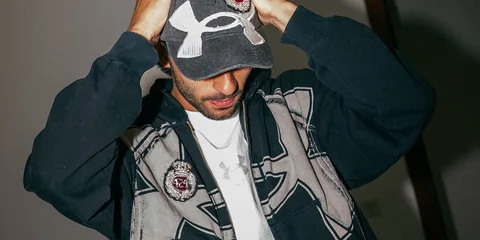 Homme portant une casquette et un sweat à capuche, regard vers le bas.