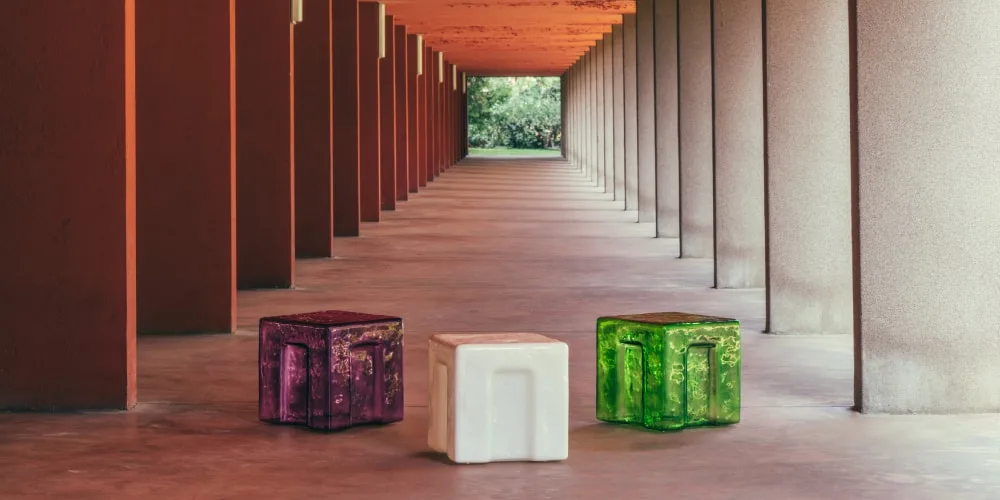 Trois cubes colorés dans un couloir moderne avec colonnes rouges.