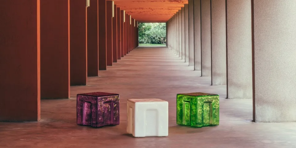 Trois cubes colorés dans un couloir moderne avec colonnes rouges.