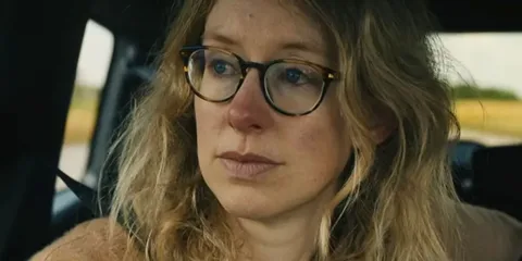 Femme aux cheveux blonds bouclés et lunettes dans une voiture.