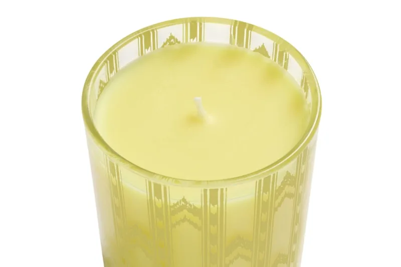 Bougie jaune dans un verre transparent avec motifs décoratifs.