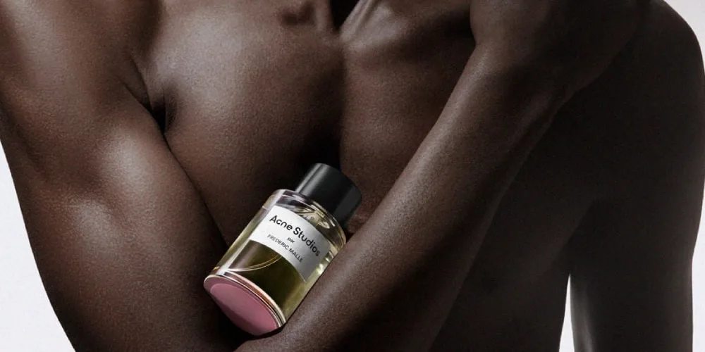 Homme tenant un flacon de parfum Acne Studios sur sa poitrine.