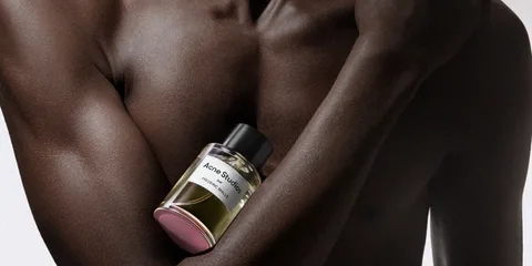 Homme tenant un flacon de parfum Acne Studios sur sa poitrine.