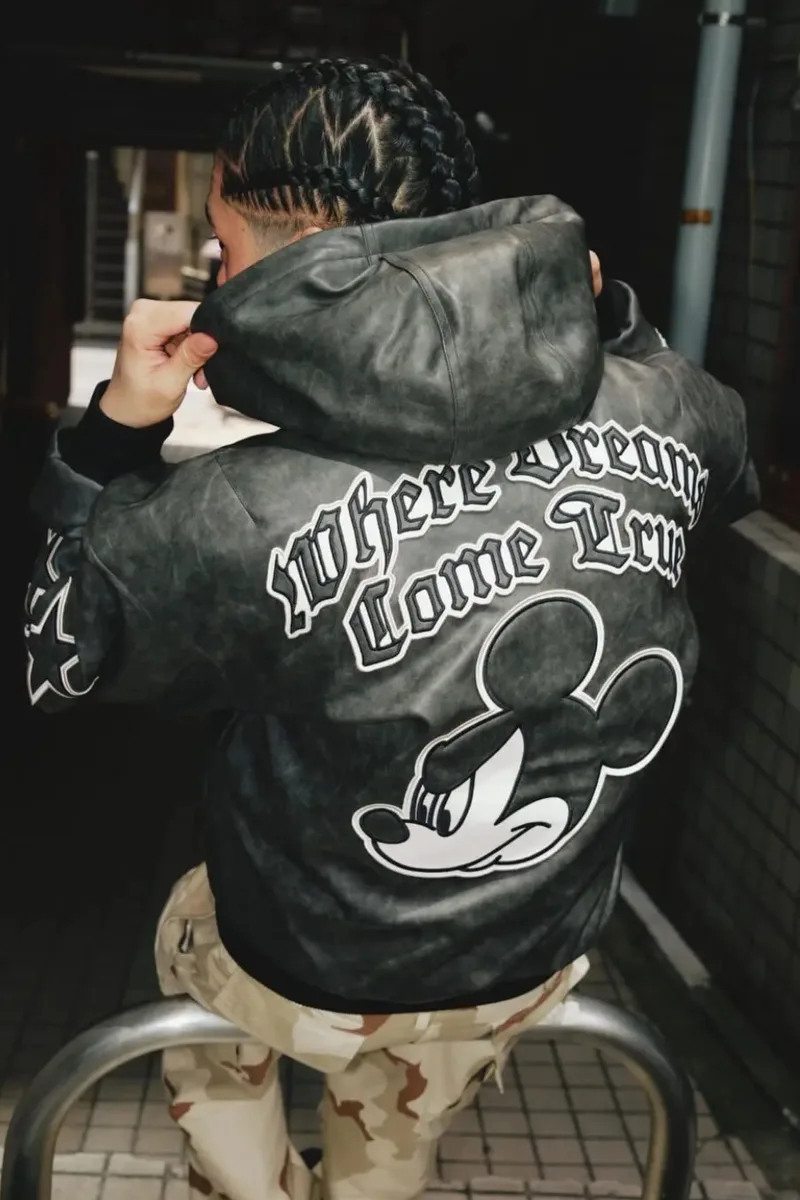 Personne portant une veste noire avec Mickey Mouse dans une ruelle.