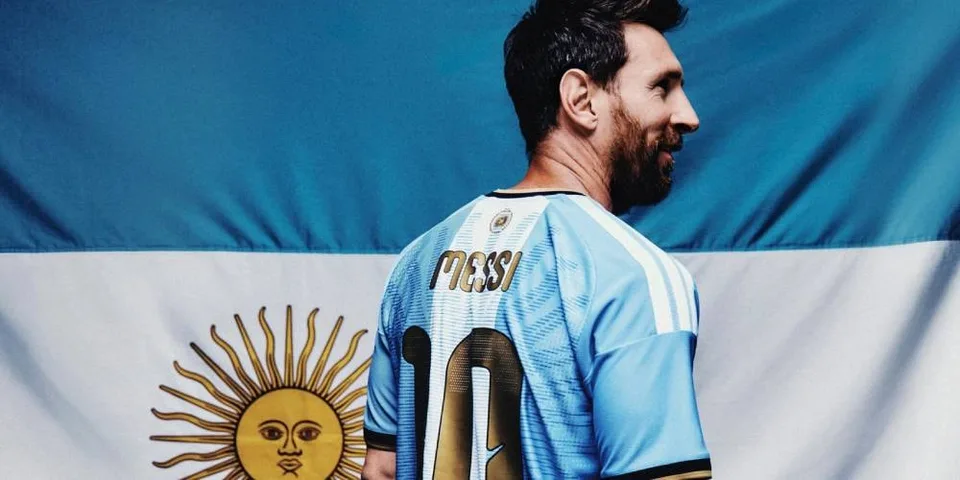 Joueur de football en maillot argentin devant un drapeau argentin.