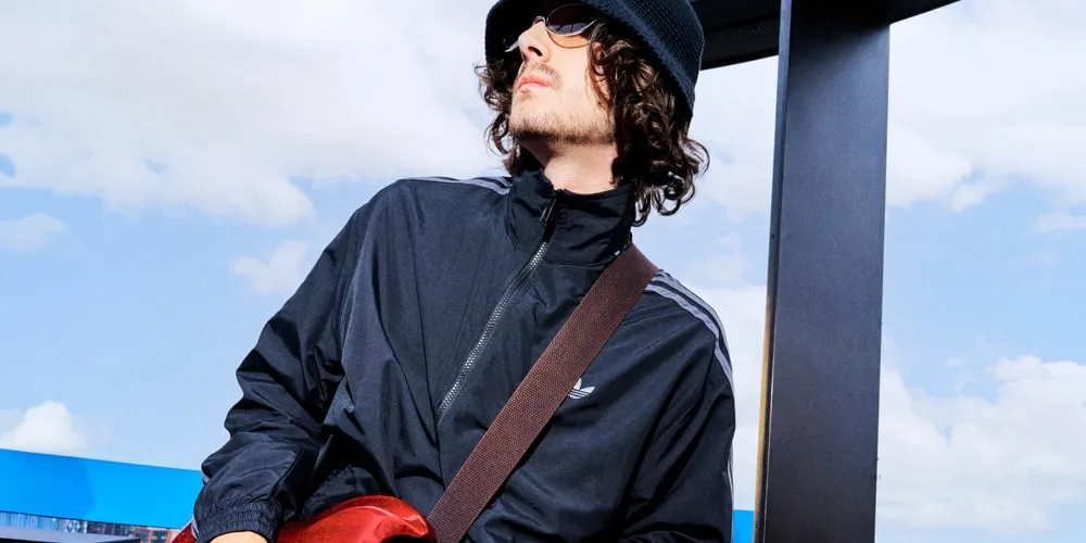 Jeune homme en bonnet et lunettes de soleil, vêtu d’une veste noire en extérieur.