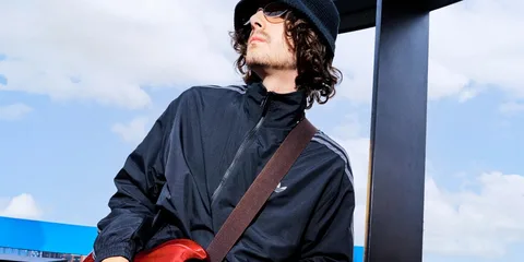 Jeune homme en bonnet et lunettes de soleil, vêtu d’une veste noire en extérieur.