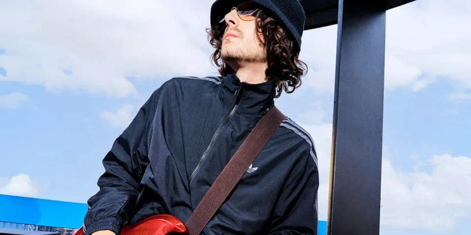 Jeune homme en bonnet et lunettes de soleil, vêtu d’une veste noire en extérieur.
