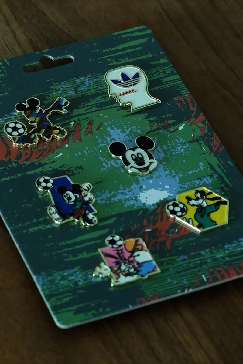 Cinq pins colorés Mickey avec motif foot sur fond vert.