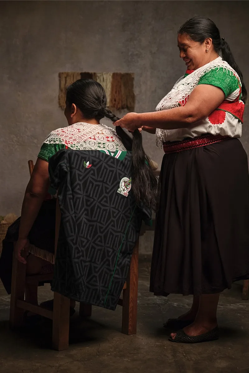 Deux femmes en tuniques traditionnelles, une tresse les cheveux de l'autre.