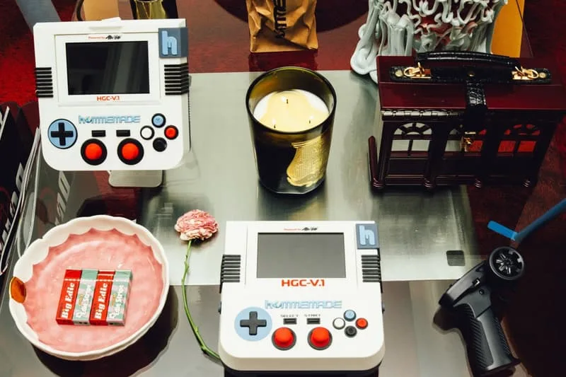 Deux consoles rétro, bougie et contrôleur sur une table.