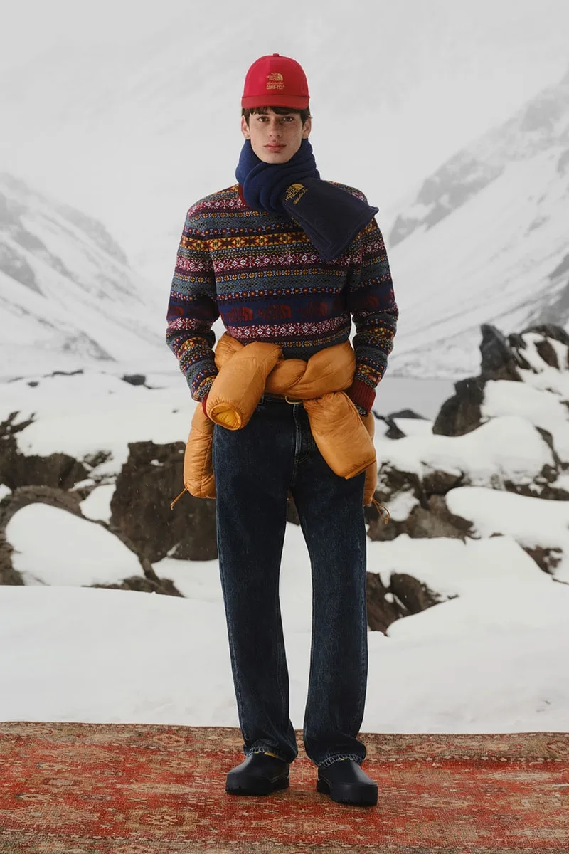 Homme en tenue d'hiver colorée avec bonnet rouge et écharpe, fond montagneux enneigé.