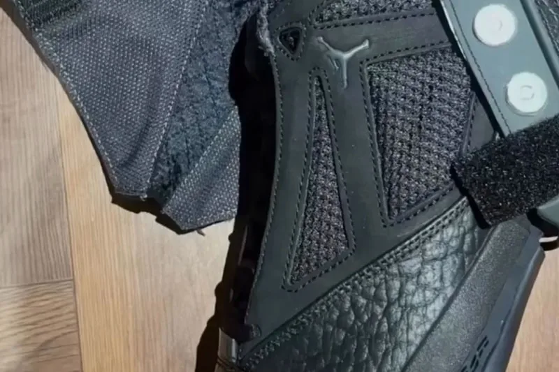 Chaussure noire avec détails en cuir et parties ajourées, sur plancher en bois.