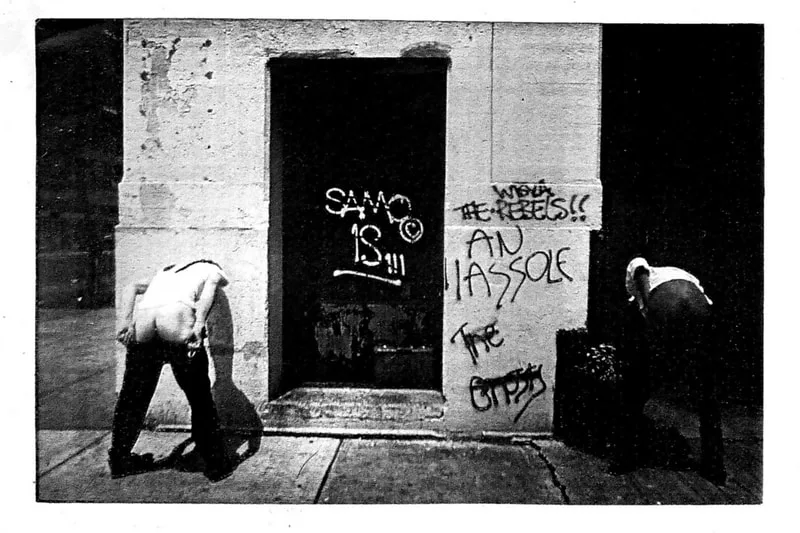 Deux personnes de dos devant un mur avec graffitis en noir et blanc.