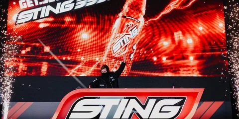 Personne levant une boisson énergisante Sting sur scène avec fond lumineux.