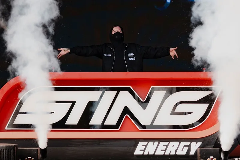 Personne masquée sur une scène avec 'STING Energy' en arrière-plan et de la fumée.