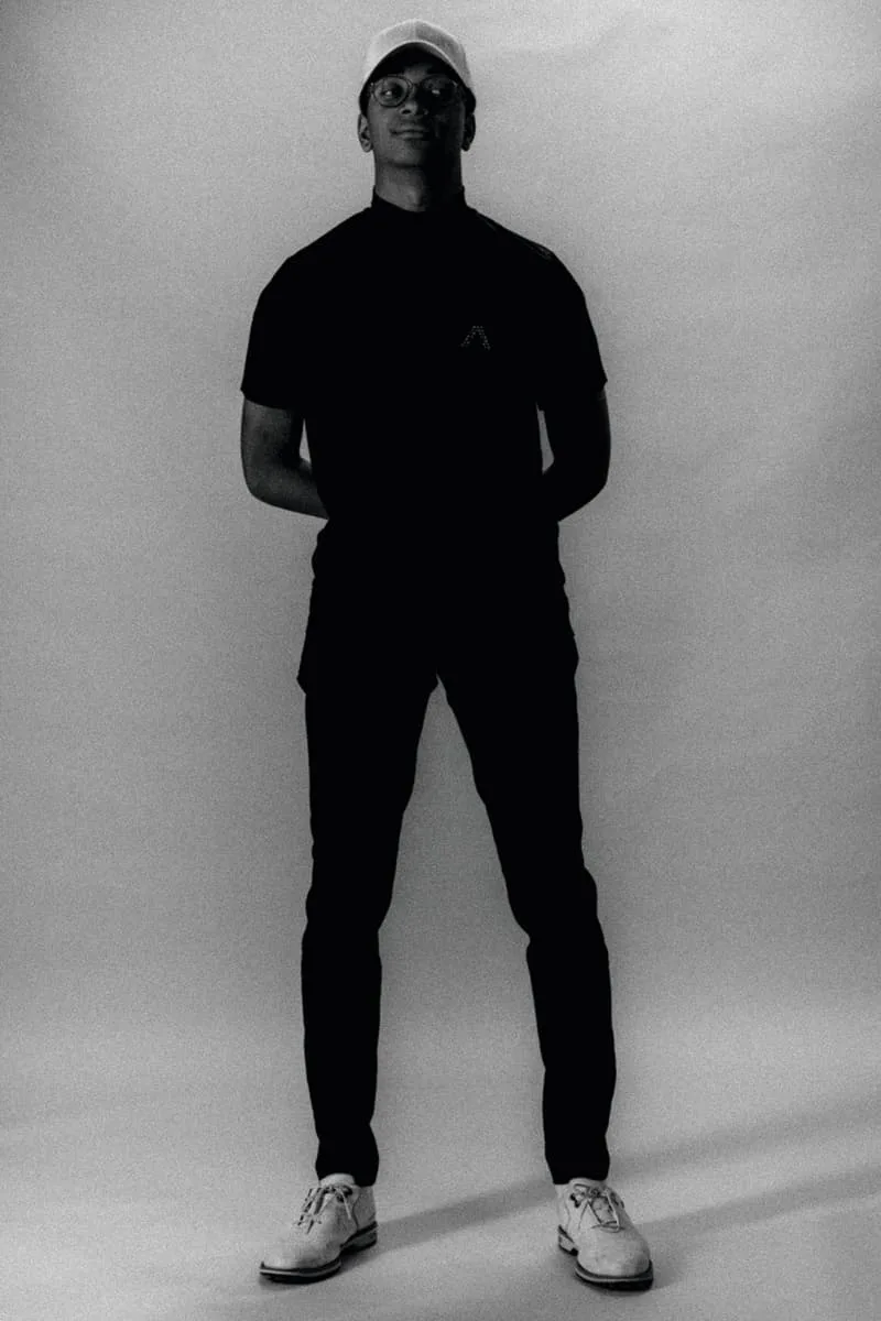 Homme debout en noir et blanc, portant casquette et lunettes.