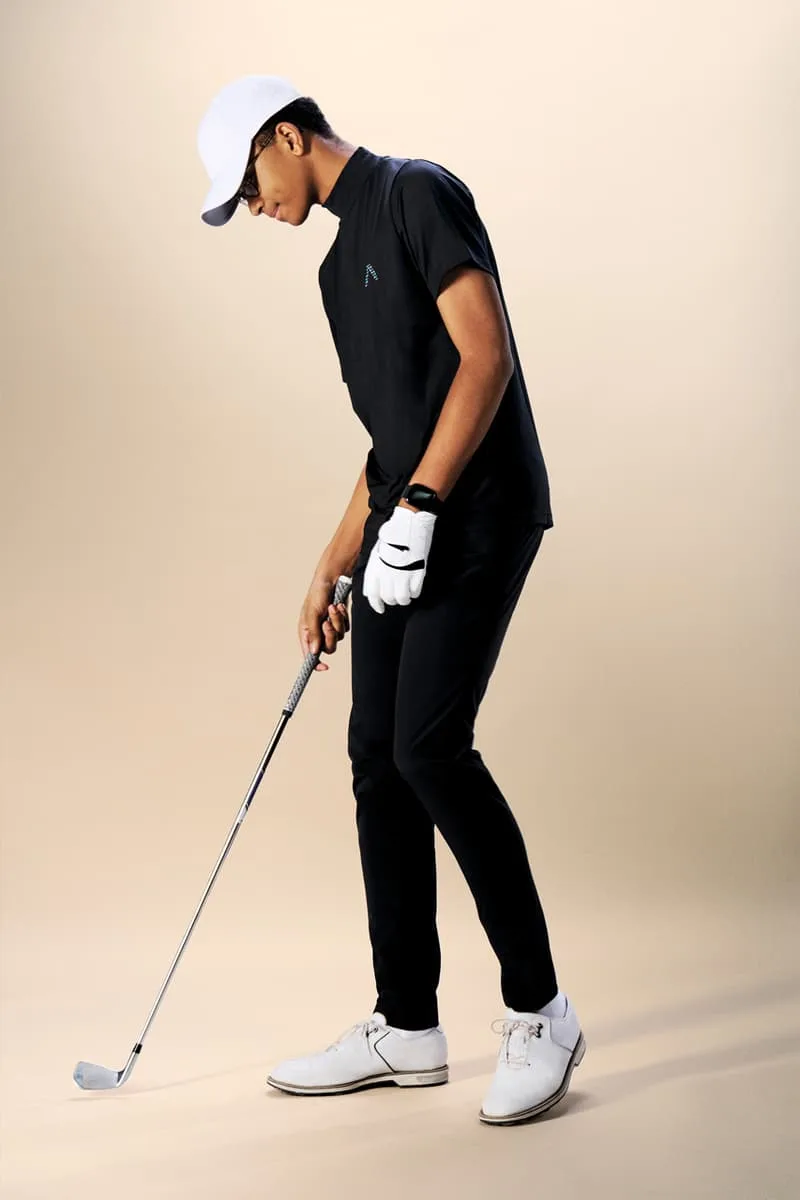 Homme jouant au golf en tenue noire, vue de profil, fond beige.