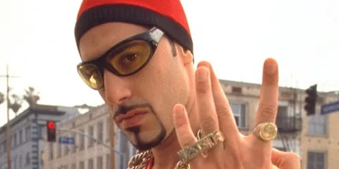Homme avec lunettes et chapeau rouge faisant un geste de main