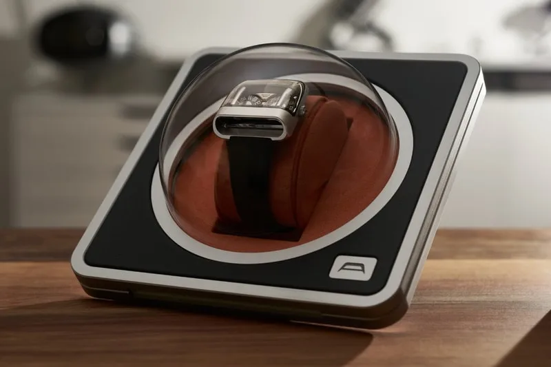 Montre exposée sous un dôme transparent sur une présentation en bois.