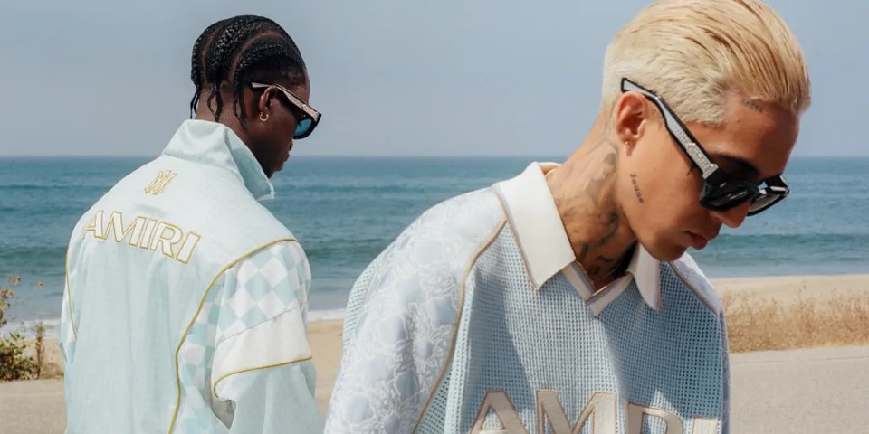 Deux hommes en tenue AMIRI près de la mer, style urbain.