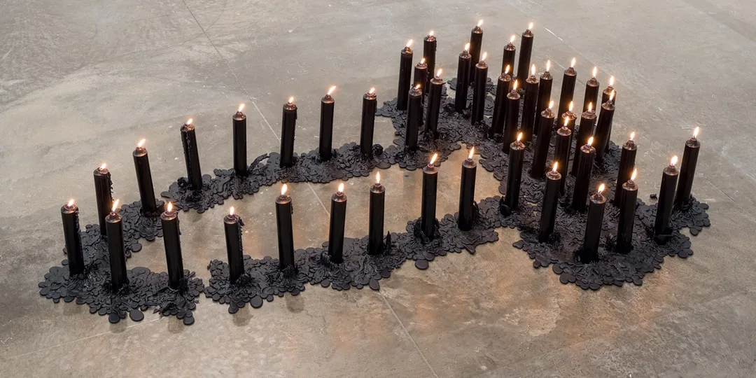 Installation de bougies noires allumées, disposées en forme de motif.