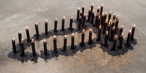 Installation de bougies noires allumées, disposées en forme de motif.