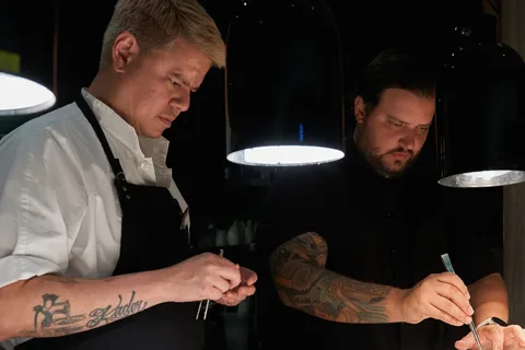 Deux chefs cuisinent sous des lampes noires.