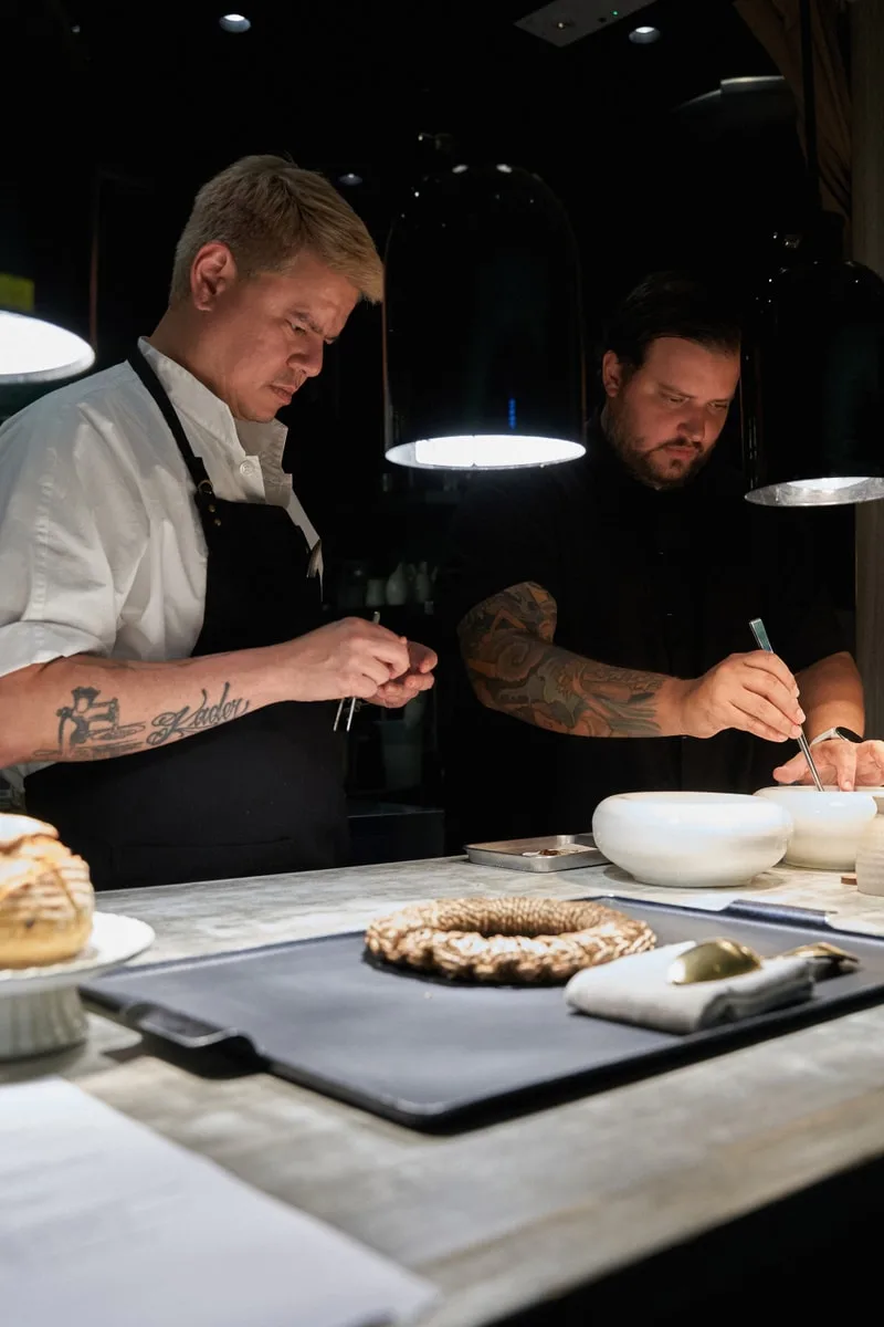 Deux chefs préparent des plats dans une cuisine professionnelle.