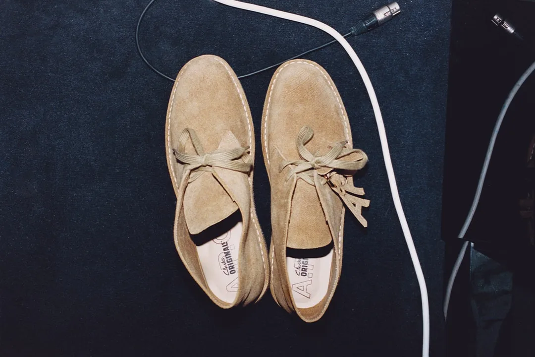 Paire de chaussures beiges avec lacets, sur un sol noir avec un câble blanc.