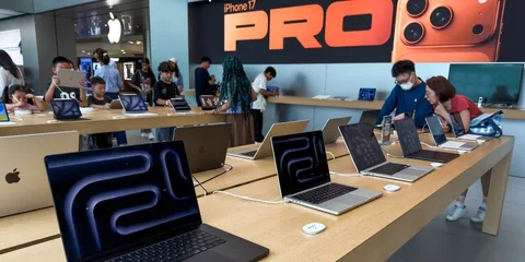 Magasin Apple avec ordinateurs et clients, affiche iPhone à l'arrière-plan.