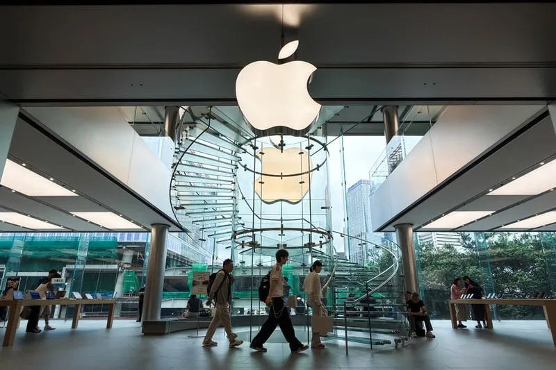 Intérieur d'un magasin Apple avec logo lumineux et escalier en colimaçon.