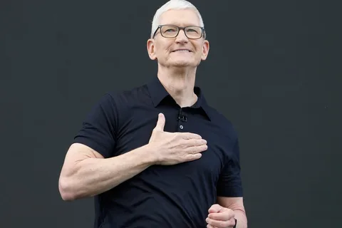 Homme portant des lunettes et un polo noir sur fond uni.