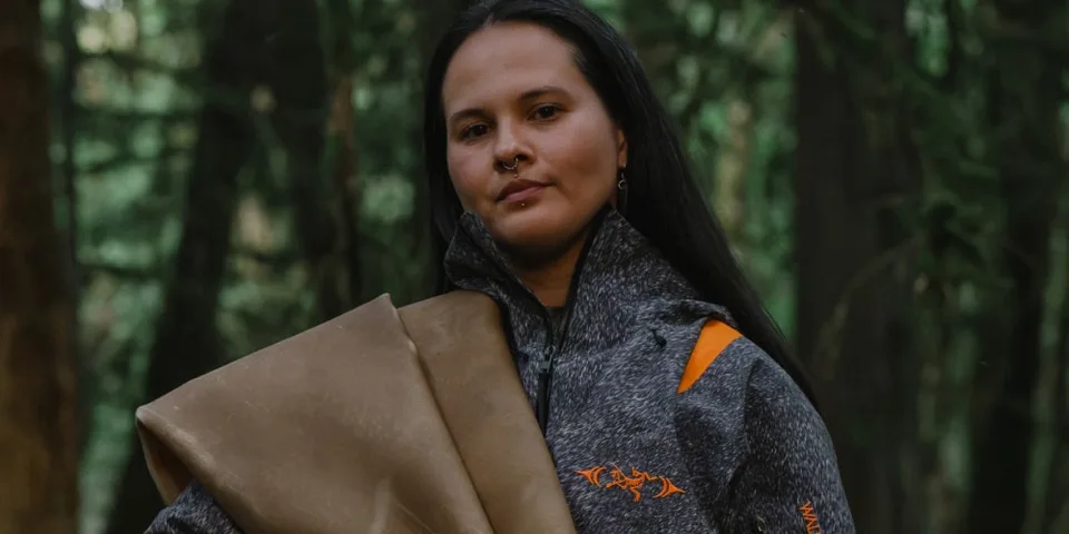 Une femme portant une veste grise se tient dans une forêt.