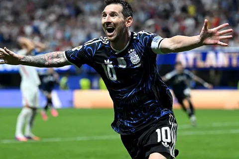 Joueur de football en maillot bleu levant les bras sur le terrain.
