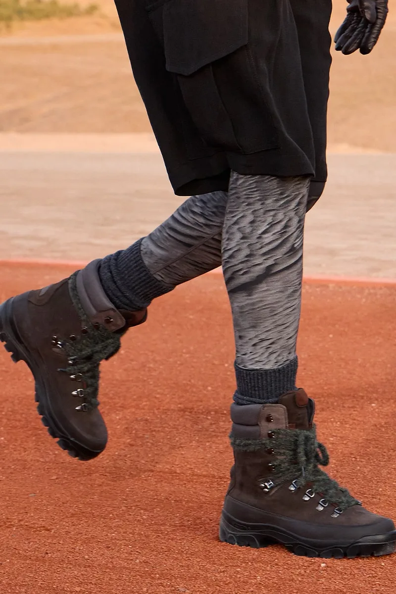 Jambes en shorts avec bottes de randonnée sur terrain rouge.