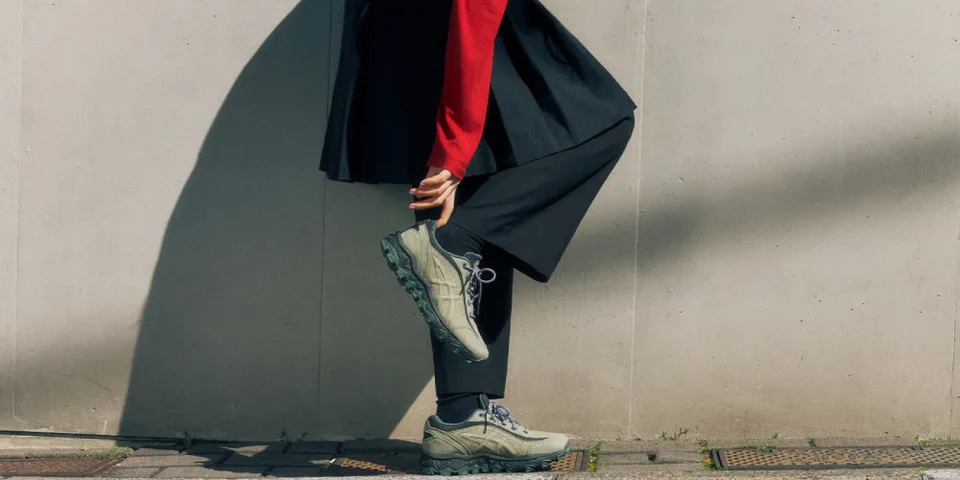 Personne tenant une chaussure beige, vêtue de rouge et noir.