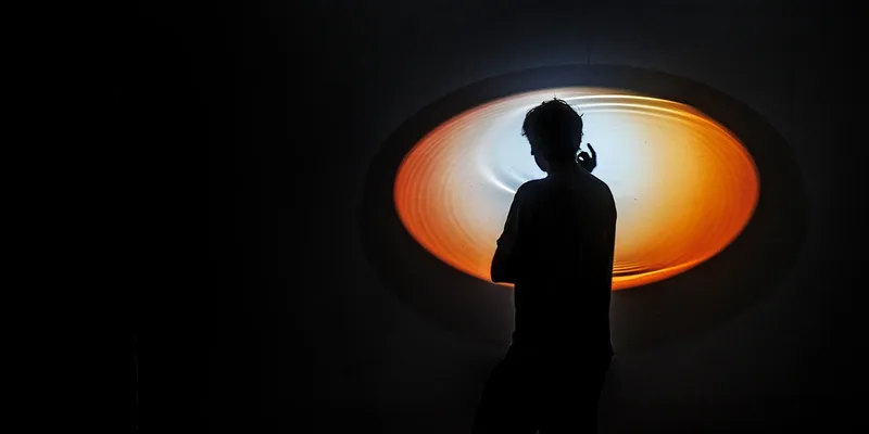Silhouette d'une personne devant un cercle lumineux orange.