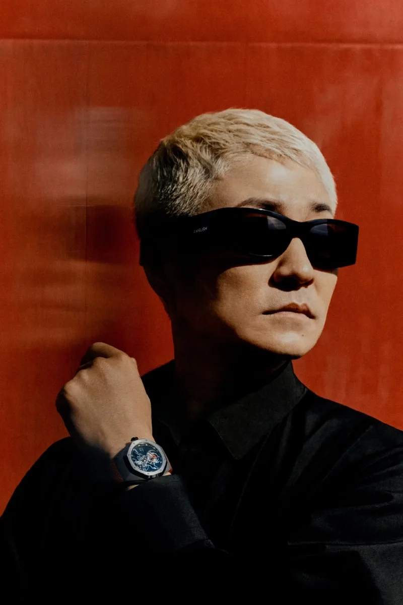 Personne avec lunettes de soleil et montre, fond rouge.