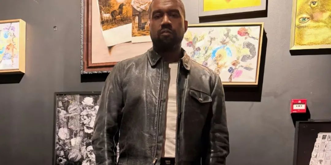 Homme en veste en cuir devant des œuvres d'art sur un mur sombre.