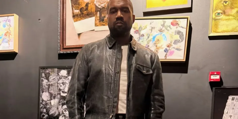 Homme en veste en cuir devant des œuvres d'art sur un mur sombre.