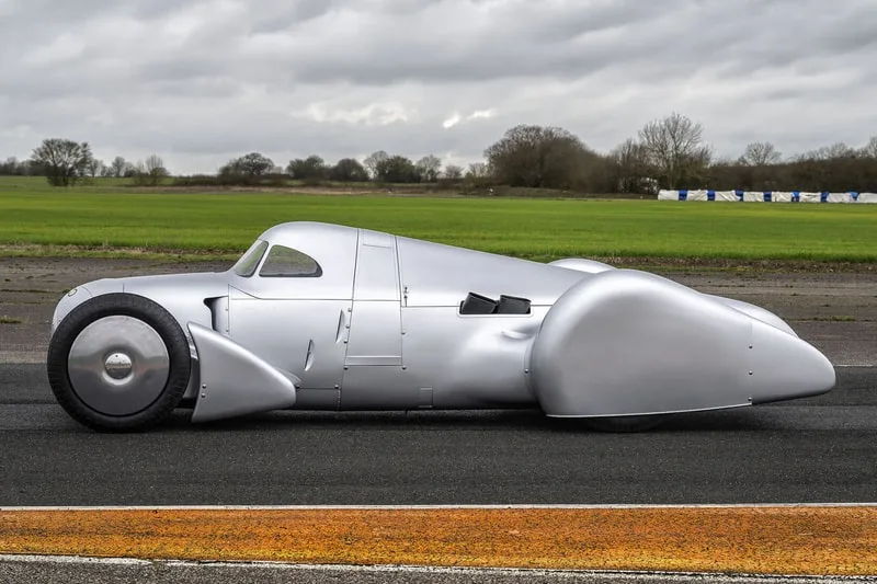 Voiture ancienne argentée sur piste, style aérodynamique.