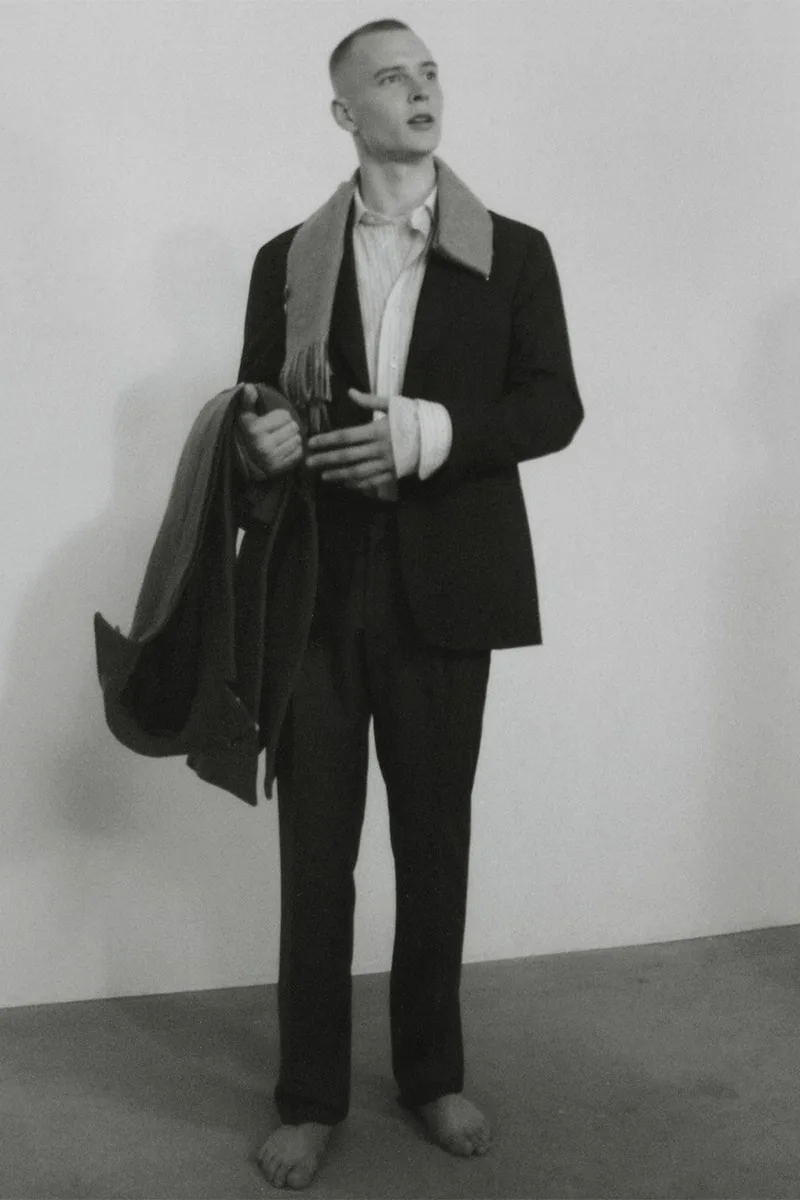 Homme pieds nus en costume tenant un manteau, pose élégante.