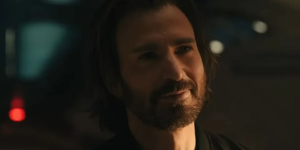 Portrait cinématographique d’un homme barbu aux cheveux longs dans une pièce sombre.