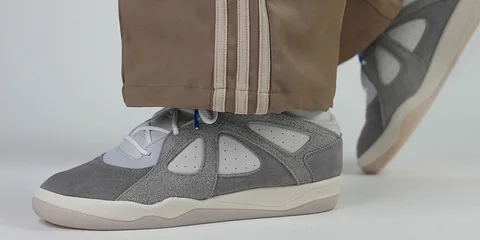Gros plan sur des baskets grises et beiges portées avec un pantalon brun.