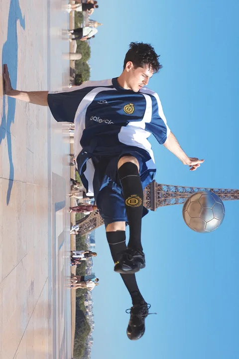 Joueur en action devant la Tour Eiffel, ballon et maillot de foot.