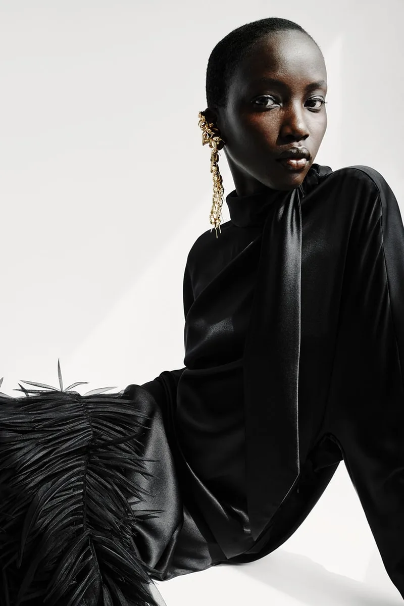 Personne posant en noir avec une coiffure unique et une boucle d'oreille dorée.
