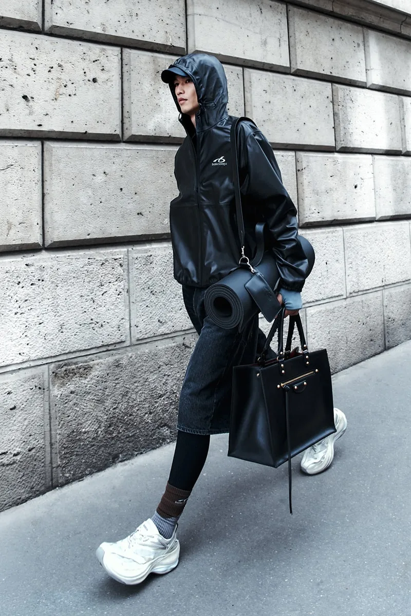 Personne avec manteau noir et sac marchant sur un trottoir.