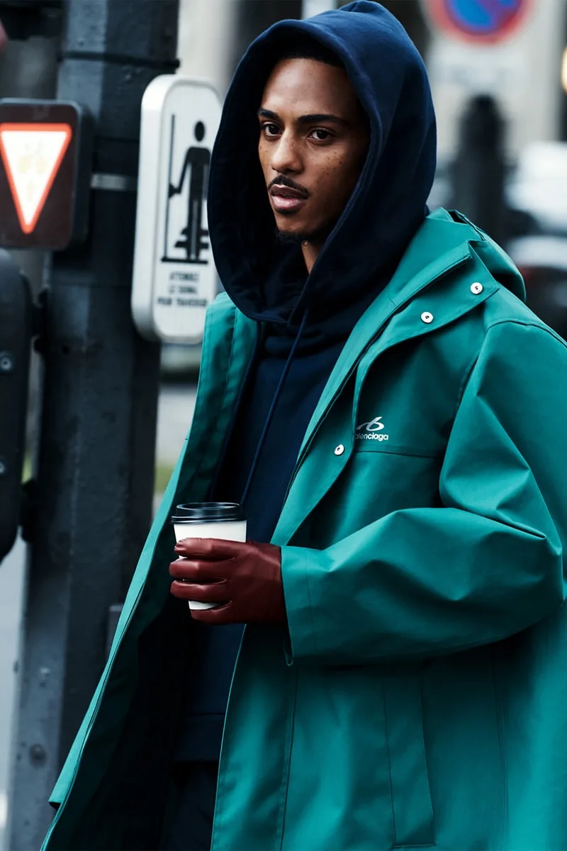 Homme avec manteau vert et gants rouges tenant un café